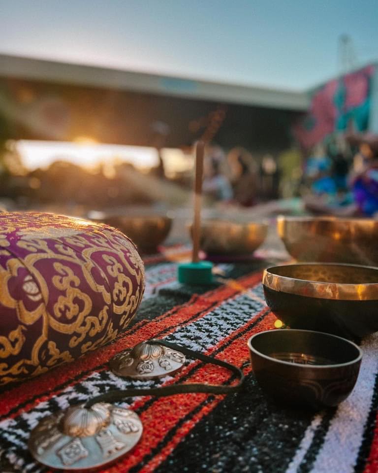 Singing bowls and tingsha chimes laid out on a woven blanket at sunset