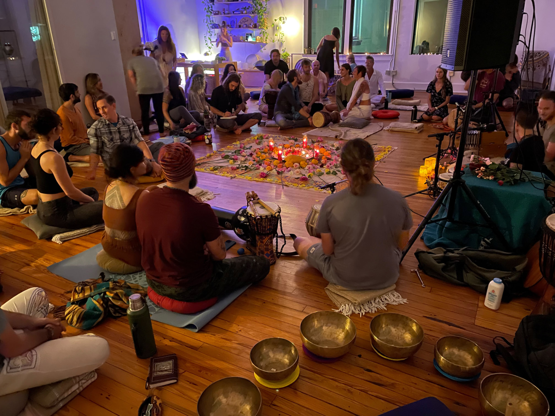 A candlelit ceremony circle with drums, flowers and singing bowls