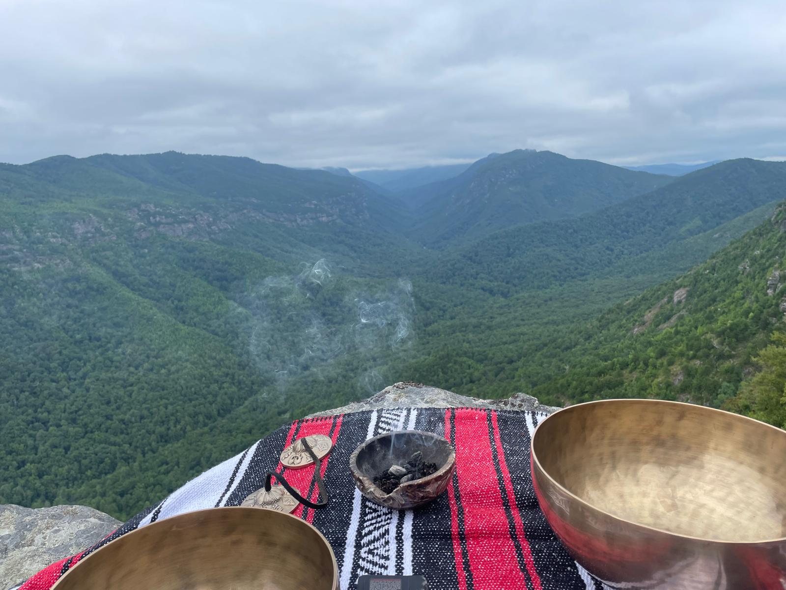 Singing bowls and smoking incense set on a blanket overlooking a mountain valley
